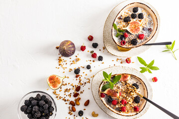 yogurt with baked homemade granola in two ceramic trend bowls. ripe blackberries, figs to improve the taste. top view. white background. a copy space.