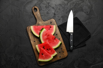 Cutting board with slices of tasty watermelon, knife and napkin on dark background