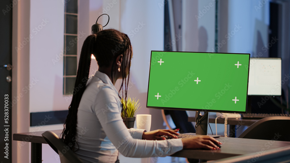 Poster african american woman looking at computer with greenscreen in office late at night. analyzing isola