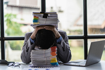A busy businessman sleeps at his desk with his financial calculators and papers piled up on a pile...