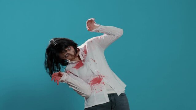Mindless and scary zombie dancing on blue background. Evil frightening brainless aggressive monster with deep and bloody wounds and scars having fun while dancing in front of camera.