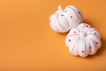 White decorative textile pumpkins with shiny stones on orange background with copy space. Autumn harvest and thanksgiving day concept