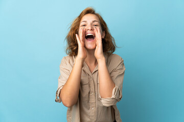 Young Georgian woman isolated on blue background shouting and announcing something