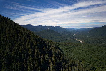 Aerial view above Gifford Pinchot National Forest of the Nisqually River twisting downstream through mountain valleys and dense forests of evergreen and deciduous trees on a cloudy summer afternoon.