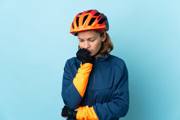 Young cyclist woman isolated on blue background having doubts