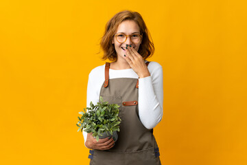 Young Georgian woman holding a plant isolated on yellow background happy and smiling covering mouth with hand