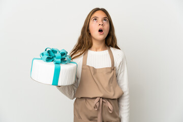 Little girl holding a big cake over isolated white background looking up and with surprised expression