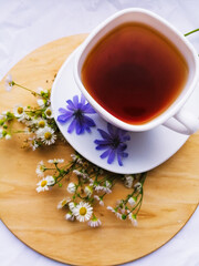 white cup of brown black tea on a wooden stand with chicory and chamomile flowers. Evening tea party.