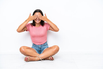 Fototapeta premium Young caucasian woman sitting on the floor isolated on white background covering eyes by hands