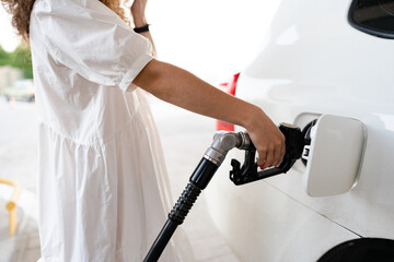 Fototapeta Close up of a woman in white dress refueling her car in a gas station obraz