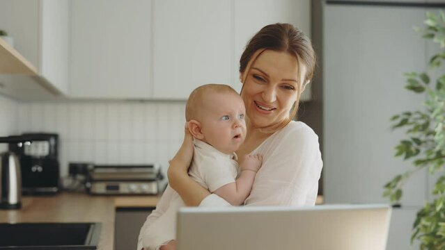 Smiled Caucasian Mother Holding The Newborn Baby Making Video Call With Her Parents Or Friends And Showing The Baby And Waving Hi To Them. Technology And Motherhood Concept