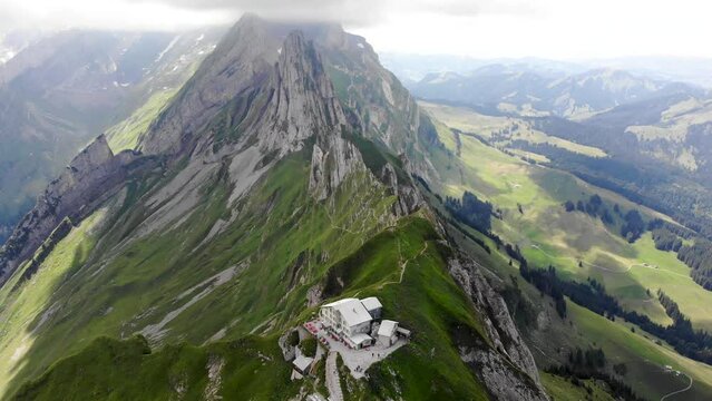 Aerial flyover towards the cliffs of Schafler ridge in Appenzell, Switzerland with mountain hut, mountain peaks and lush green mountainsides in view
