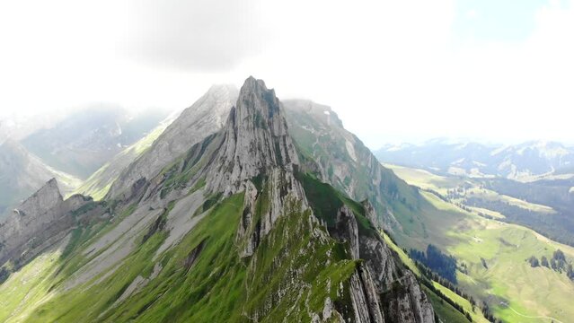 Aerial flyover over the cliffs of Schafler ridge in Appenzell, Switzerland towards Altenturm peak on a cloudy summer day with a view of one of Switzerland's most popular, yet dangerous hiking trails