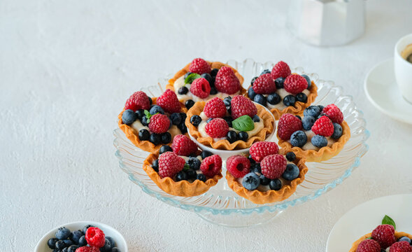 Tartlets with custard, fresh raspberries and blueberries on a light concrete background. Recipes with custard and berries. Confectionery