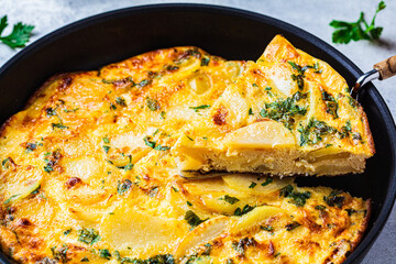 Traditional Spanish potato tortilla or omelette in black pan.