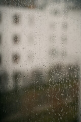 Raindrops on a window with an apartment house background. Concept of staying home while there is bad weather outside. Cozy indoor view at rainy weather