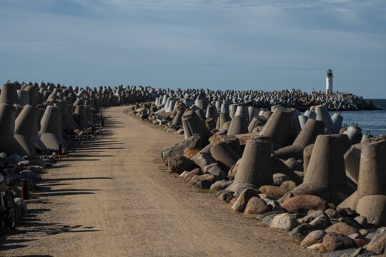 Trail leading to a lighthouse with wave breakers on the side during the day