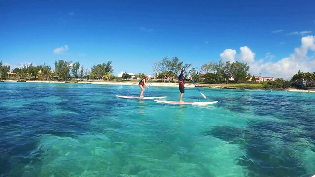 Man and woman paddling on a Stand up Paddle (SUP) in Mauritius in front of a beautiful beach and palm trees