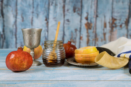 Jewish New Year traditional symbols with shofar glass honey jar, fresh apples, and pomegranates celebrating Rosh Hashanah
