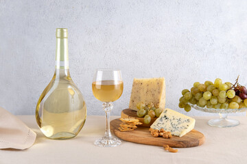 Glass and bottle of white wine with blue cheese and grapes on light background. White wine with...