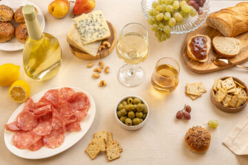 Glasses and bottle of white wine with grapes, cheese and salami on light table background. White wine with cheese and fruits. Wine bottle mockup with blank labels to place your design. Space for text