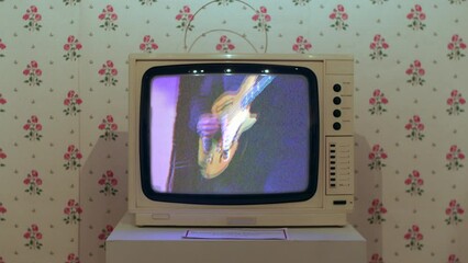 A 1980s white television set. The tv is displaying a VHS music video