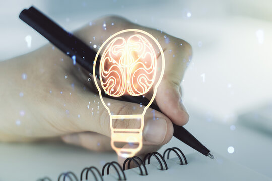 Creative light bulb with human brain hologram and with man hand writing in notepad on background, artificial Intelligence and neural networks concept. Multiexposure