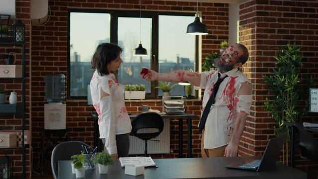 In love spooky romantic brain-eating zombie man proposing to his creepy girlfriend. Two apocalyptic undead monsters with deep bloody wounds getting married in office workspace.