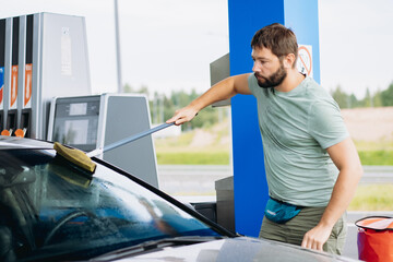 man washing windshield of car at gas station