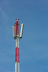 Red white telecommunication tower with antennas on a blue sky