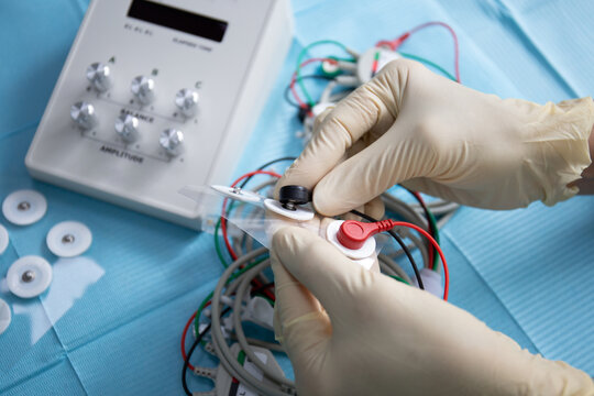 Doctor's hands connect electrodes for tensotherapy device in dentistry close-up.