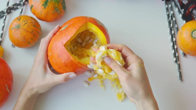 Girl preparing a scary pumpkin in autumn holidays. Woman making the Halloween attribute with your hands. Hands take out pumpkin seeds. Jack-O-Lantern creation. Do it yourself - creative realisation