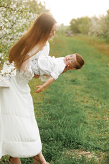 Obraz premium Portrait of happy mother and her baby boy. Beautiful touching scene of mom and son. Blooming garden in spring.