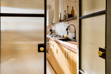 Stylish and sunny kitchen interior of modern apartment made in white and beige tones. View through the opened glass door