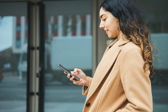 Young Woman Using Smart Phone By Building