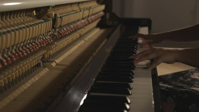 Woman playing upright piano with open sound board showing hammers striking the strings