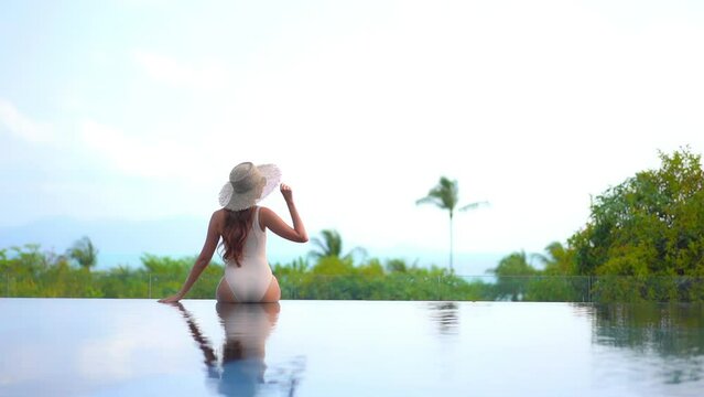 Back View of Lonely Sexy Woman Sitting on Infinity Pool Edge With Stunning View of Tropical Island and Sea Horizon