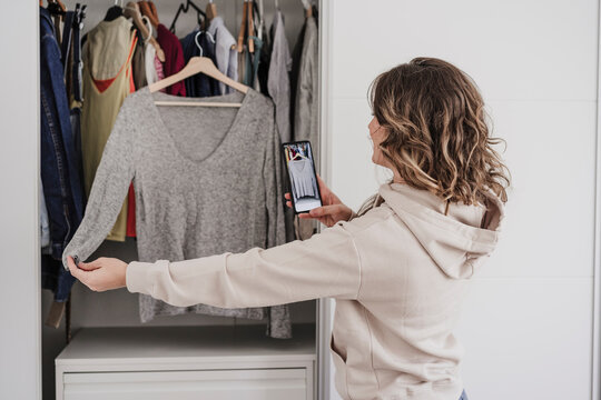 Woman photographing top through mobile phone hanging in wardrobe
