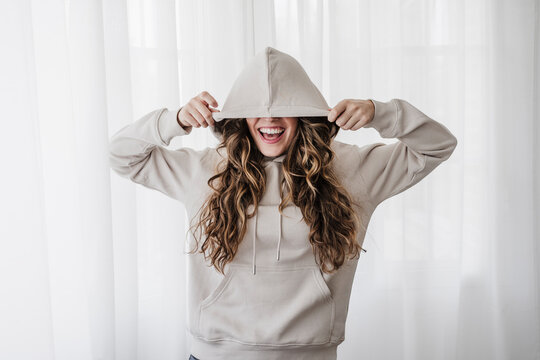 Playful woman covering eyes with hood at home
