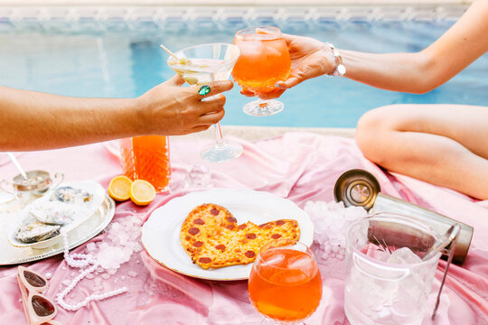 Friends toasting cocktails over heart shaped pizza at poolside