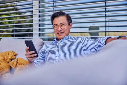 Smiling Mature Man With Smart Phone Sitting On Sofa