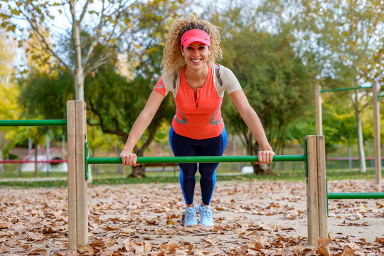 Happy sportswoman practicing push-ups on horizontal bar at park