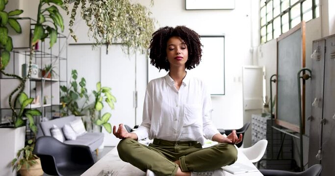 Young businesswoman meditating cross-legged on office table