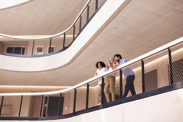 Business colleagues leaning on railing in corridor