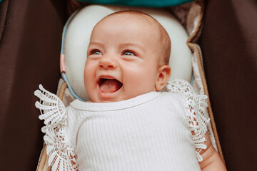 Close-up portrait of happy smiling newborn baby girl lying in pram. 3 month old infant with blue...