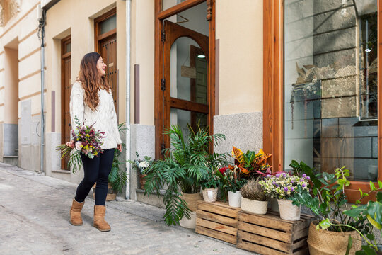 Smiling woman with bouquet walking by flower shop