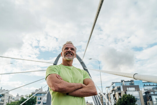 Smiling man with arms crossed standing on bridge in city