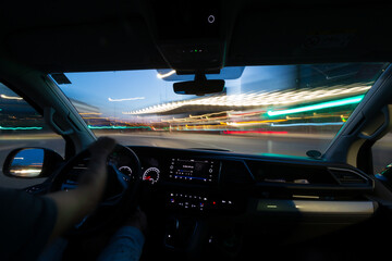 Interior view of a person driving a car with long exposure light trails.