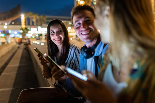Happy young man and woman holding mobile phones talking with friend at night