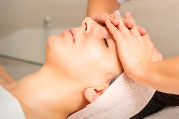 Fototapeta na wymiar Facial massage. Young caucasian woman with closed eyes getting a massage on her forehead in a beauty salon